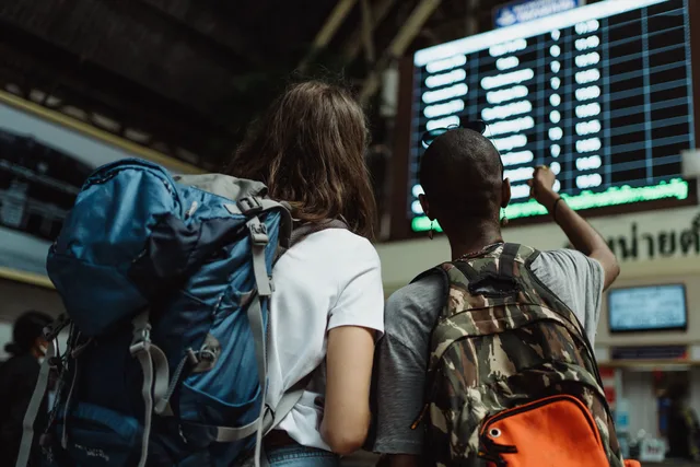 Two backpackers checking the digital board at a train station for travel information. Så hanterar du aviseringar vid förseningar och avvikelser