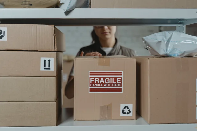 A person organizing fragile cardboard boxes in a warehouse setting. Så sätter du leveranstider och cutoff-tider